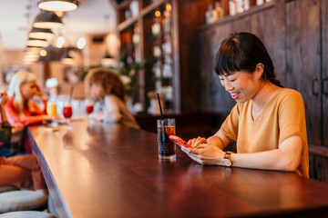 Young woman using smartphone and drinking cocktail in bar