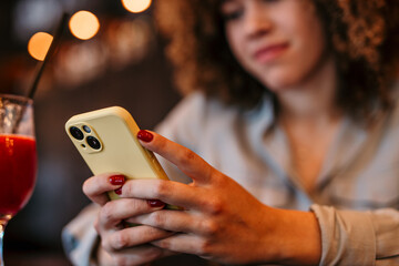 Woman using smartphone in restaurant, browsing social media and enjoying beverage