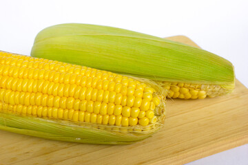 Two fresh sweet corns on the wooden board, isolated on white background.