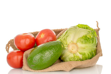 Three red tomatoes, one avocado and cabbage in a jute bag, close-up, isolated on a white background.