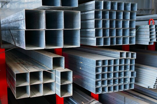 Industrial storage of building metal profiles. The warehouse is filled with a large number of new galvanized hollow square steel beams, each 6 meters long.