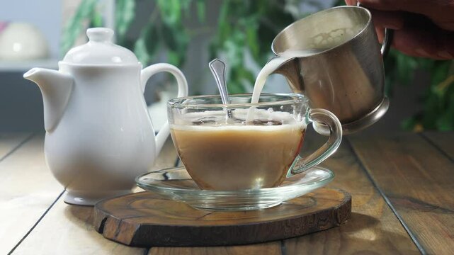 An elderly man pours milk into a cup of hot coffee. Close-up. Slow motion.