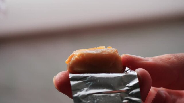 Unwrapping a Caramel Candy, close-up shot of fingers unwrapping a soft, golden caramel candy from its silver foil wrapper