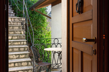 Open front door of an apartment leading to a small balcony and to a staircase in the garden