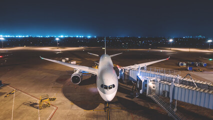 Front view of passenger commercial airplane parked at airport gate at night. ready for boarding and departure. Illuminated runway in the background. aviation, transportation, international flights.