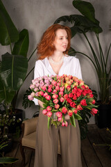 Young caucasian female holding colorful tulip bouquet indoors surrounded by lush green plants