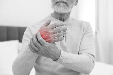 Arthritis. Senior man suffering from pain in hand at home, closeup. Black and white toning with red...