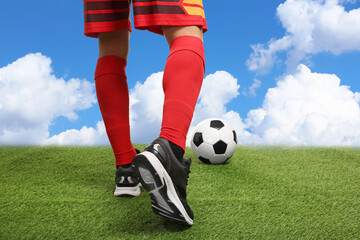 Football player kicking soccer ball under blue sky, closeup