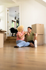 Young diverse couple sitting on floor enjoying coffee while unpacking in new home