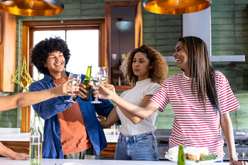 Friends toasting with wine glasses in modern kitchen, celebrating together
