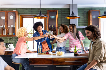 In kitchen, friends raising glasses and celebrating casual gathering together