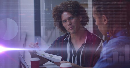 Image of lights and graphs over diverse businesspeople working in office