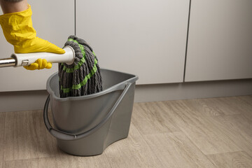 A hand holds a floor mop over a bucket of water. Cleaning concept, mop and bucket.