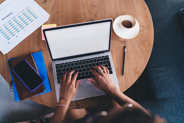 Flat lay perspective of hands on keyboard working remotely in café, with smartphone, sticky notes, coffee cup and project charts on wooden table indicating busy freelancer lifestyle