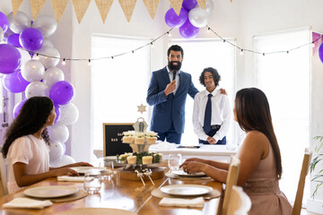 Celebrating religious milestone, diverse family giving speeches with decorations at home gathering