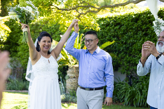 Celebrating senior wedding outdoors, joyful couple holding hands and smiling with guests