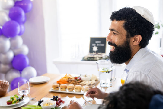 Diverse family, Smiling father wearing kippah enjoying festive meal with friends at home