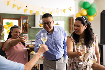 Senior friends celebrating with wine glasses at home, smiling and enjoying together
