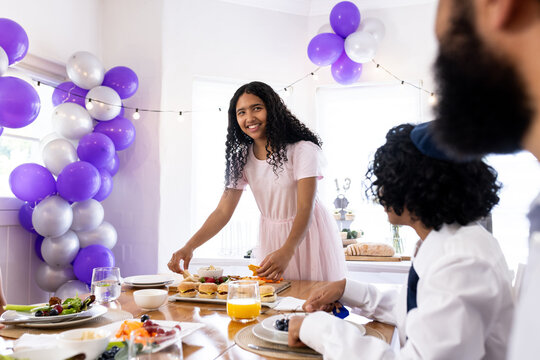 Girl setting table for festive meal with diverse family during religious celebration, at home