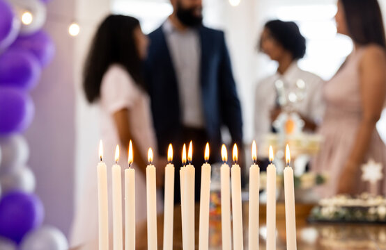 Candles burning brightly at festive gathering, people celebrating in background, at home
