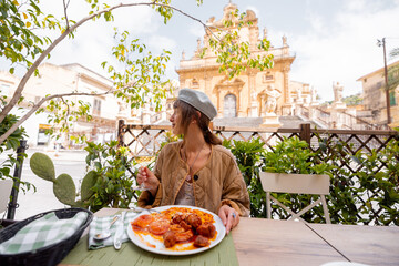 Smiling woman enjoys hearty Sicilian lunch with gnocchi, meatballs and tomato sauce, paired with...
