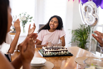 Teen girl celebrating birthday with cake and balloons, smiling with friends, at home