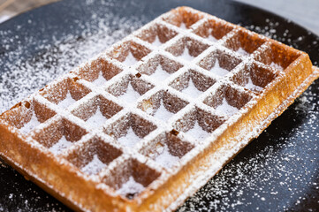Brussels waffle with icing sugar on a black plate in Hoeilaart, Flemish Brabant, Belgium