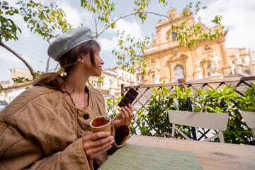 Young woman enjoying traditional Modica chocolate and hot drink at a cafe terrace with a view of...