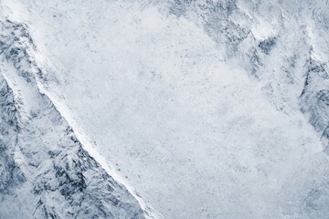 Obraz premium High-angle view of snowy mountain peaks, textured with various shades of pale blue and gray, creating a rugged, icy landscape