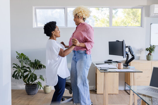 Two friends dancing joyfully in home office, enjoying fun break together