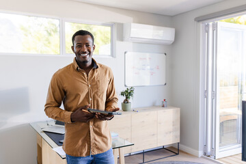 Smiling man holding tablet in modern home office, enjoying work environment