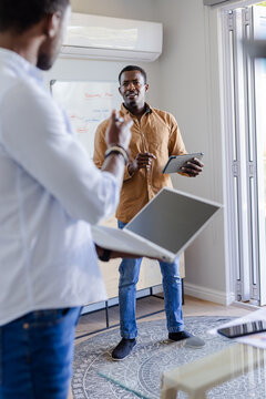 Collaborating at home, two men discussing project using tablet and laptop
