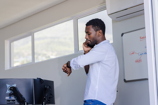 Businessman checking watch while talking on smartphone in modern office