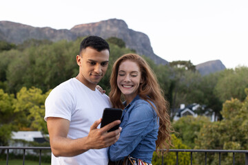 Fototapeta premium Smiling couple looking at smartphone together outdoors in sunny weather