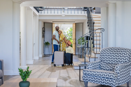 African american couple arriving home with luggage, smiling and embracing in hallway
