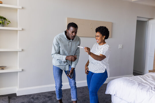 Celebrating positive pregnancy test result, African American couple looking excited at home