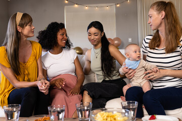 Women enjoying conversation at home, celebrating with snacks and baby present
