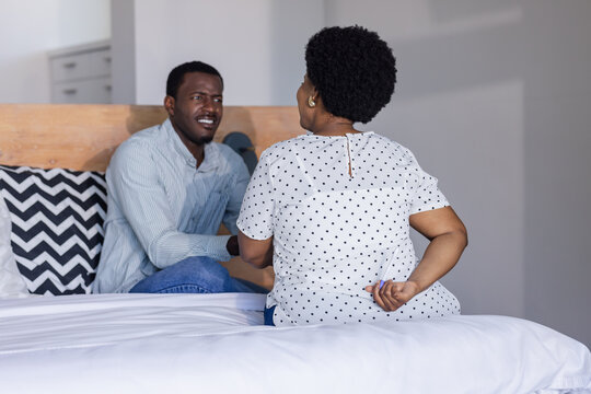African American couple sitting on bed, having heartfelt conversation at home