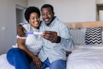 Couple sitting on bed joyfully holding positive pregnancy test, celebrating news