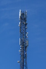 A tall communications tower equipped with antennas and satellite dishes stands sharply against a vivid blue sky, symbolizing modern technology and connectivity. Includes copy space.