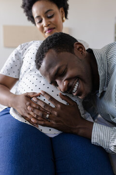 Expectant father joyfully listening to pregnant partner's belly at home