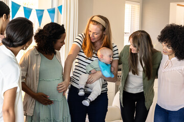 Friends celebrating baby shower, smiling and gathering around pregnant woman at home