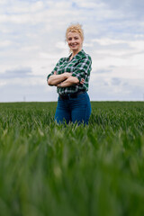 Adult female farmer standing in green wheat field looking at camera.