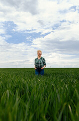 Adult female farmer standing in green wheat field.