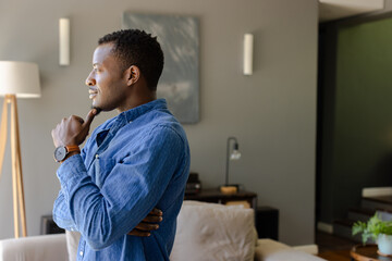 Thoughtful man in blue shirt contemplating at home, looking out window