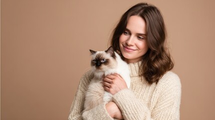 Young caucasian female smiling while holding fluffy siamese cat against beige background