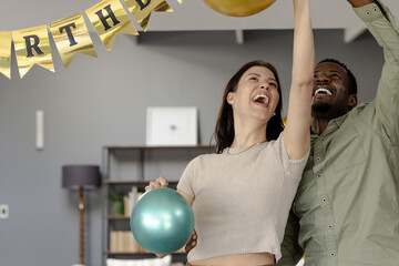 Fototapeta premium Happy couple celebrating birthday at home, holding colorful balloons and smiling