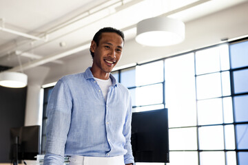 Asian man standing in open office with grid windows using computer monitors and smiling, copy space