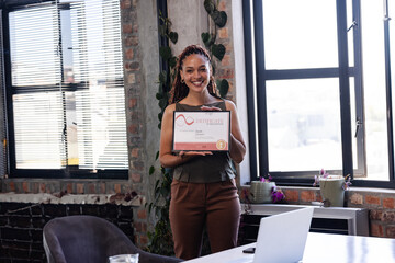 Mid adult woman standing in industrial style office loft, holding certificate and smiling