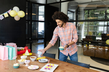 Asian man placing snack bowls, pastel gift bags on wooden table during office party, copy space